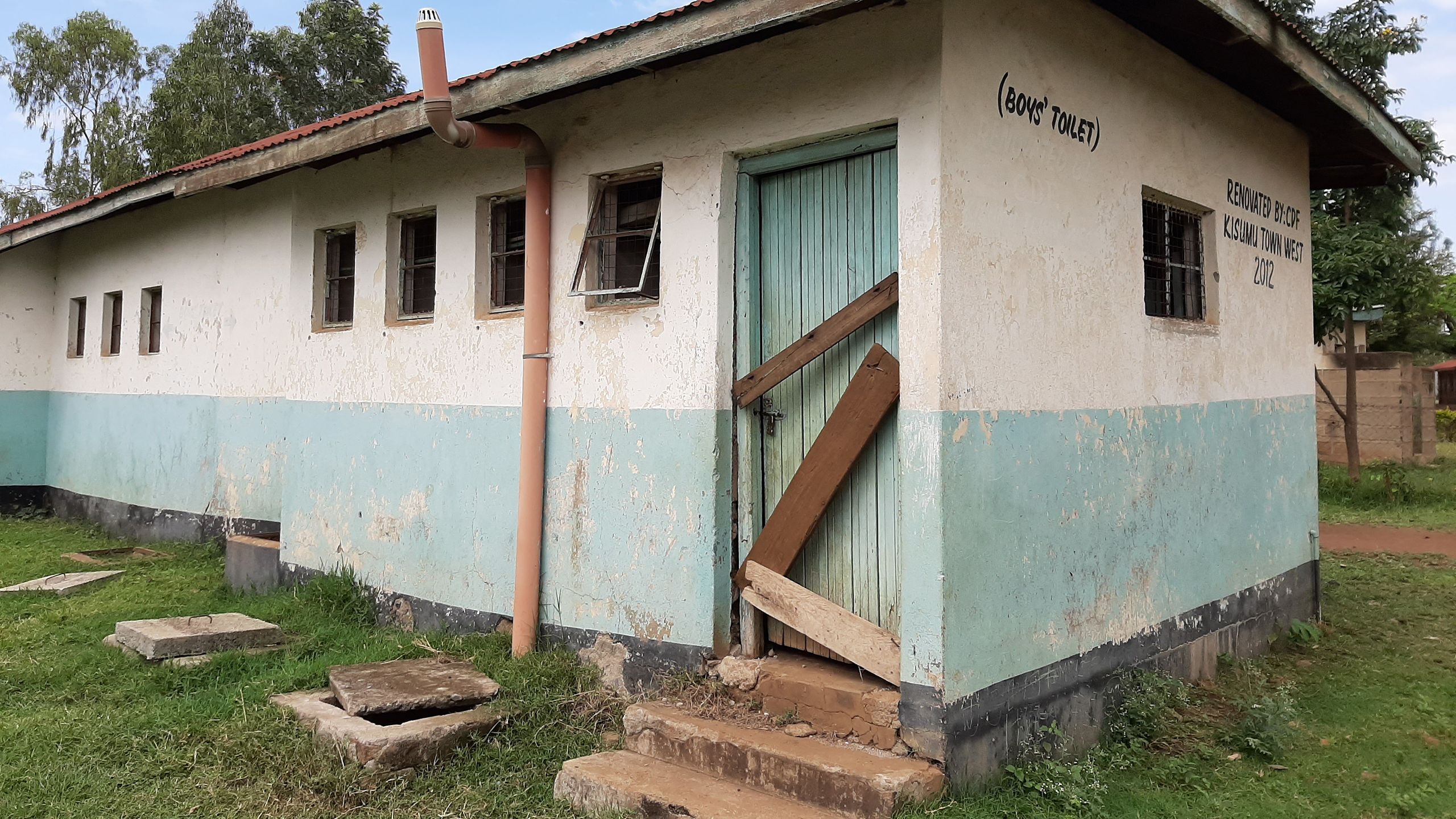 A building with wooden boards blocking a doorway. It's written "BOYS' TOILET".